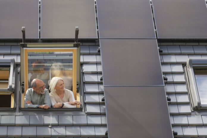Foto zeigt ein Paar am Dachfenster mit Blick auf die PV-Anlage